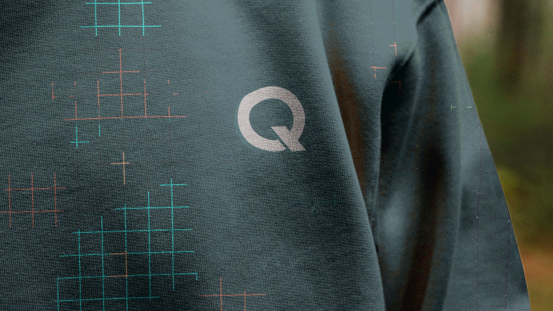 Quandry Q lockup on a teal jacket with blueprint grid